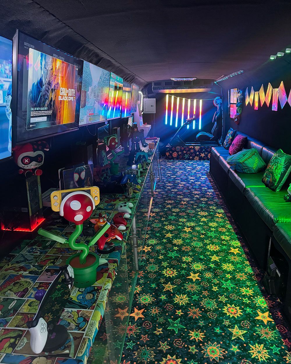 A vibrant gaming bus interior with neon-lit screens, star-patterned carpeting, a Piranha Plant prop, and bench seating.