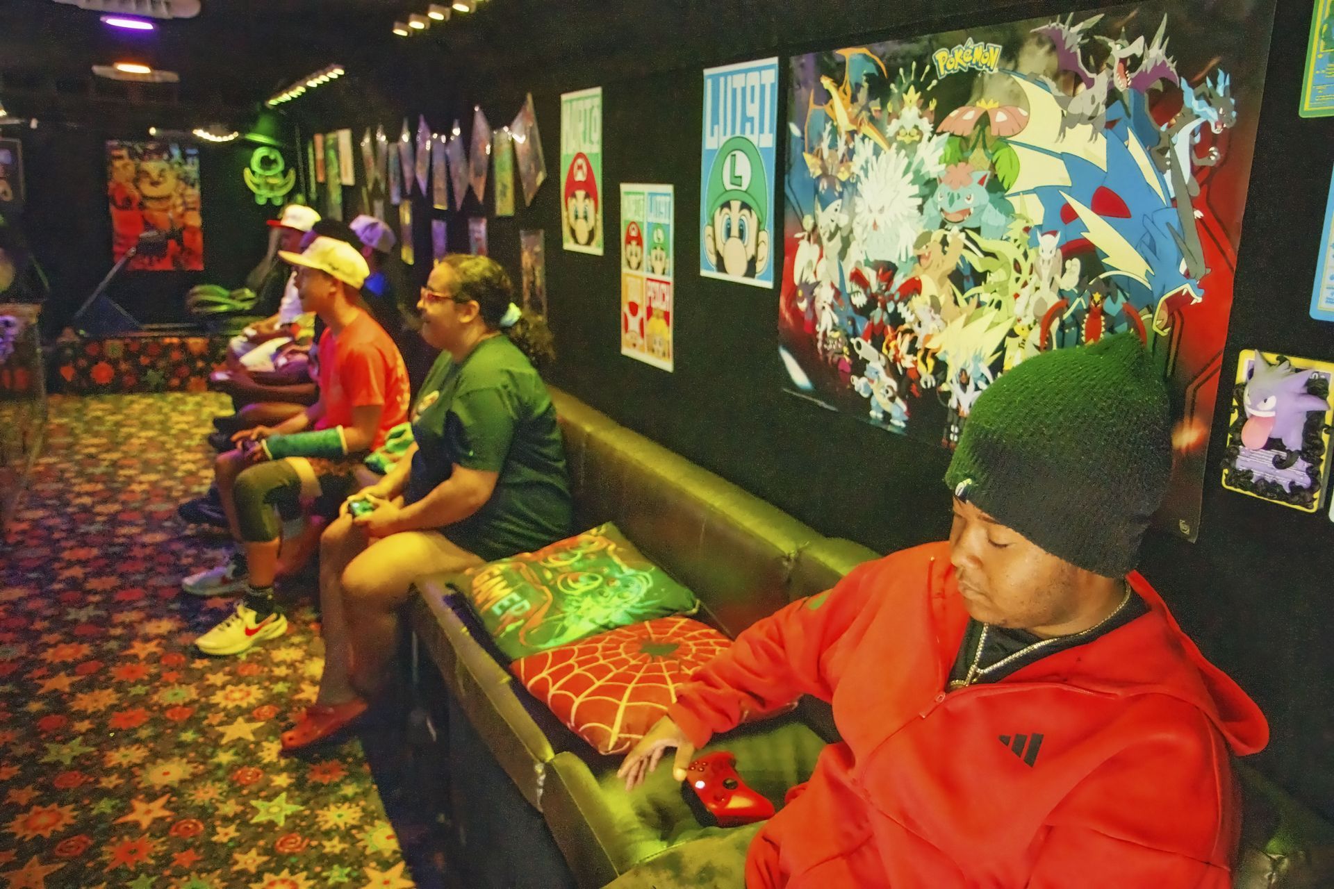 Three people sitting in a colorful arcade hallway with posters and bright patterned carpet