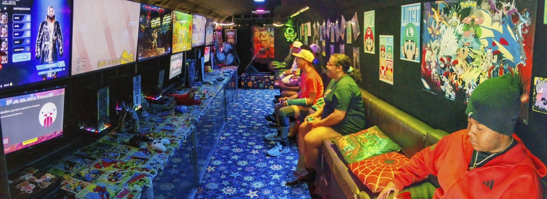 People sitting in a colorful arcade watching screens on a blue patterned floor.