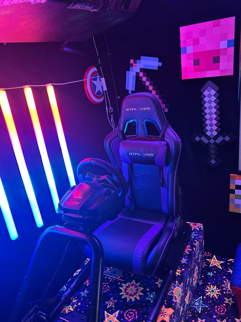 A racing game setup featuring a gaming chair and wheel, illuminated by blue neon bars against a wall with Minecraft decor.