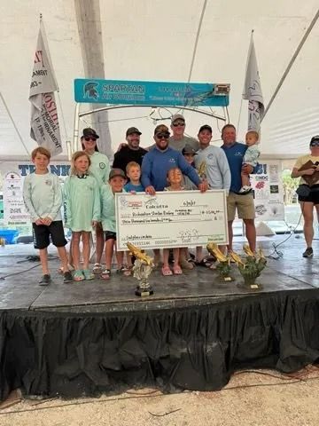 Group of people on a stage, holding a giant check. They appear to be celebrating a fishing tournament.