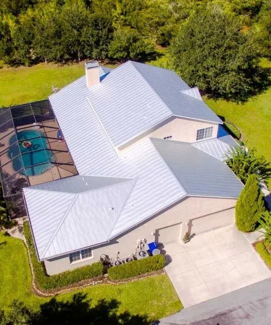 Aerial view of a house with a silver metal roof, pool, and attached garage on a green lawn.
