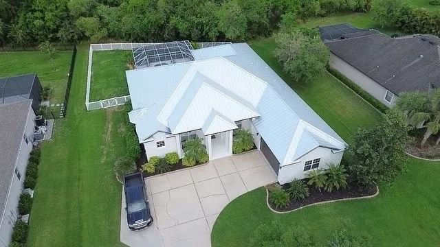 Aerial view of a white house with a silver roof, driveway, and green lawn.