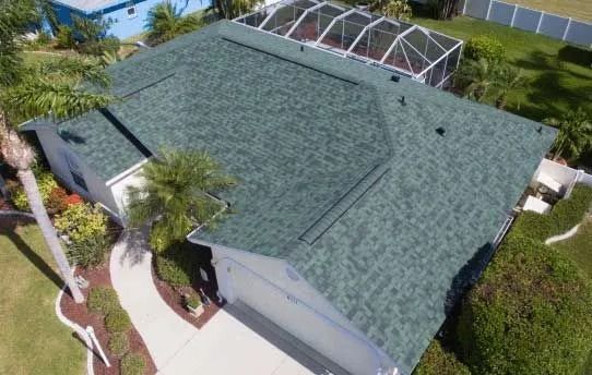 Overhead view of a house with a green shingle roof, white walls, a walkway, and a screened-in pool enclosure.