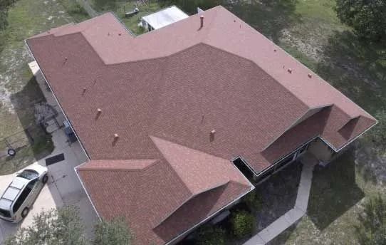 Overhead view of a house with brown shingle roof, a white car in the driveway, and surrounding trees.