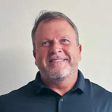 Man with short brown hair, blue eyes, smiling, wearing a black polo shirt.