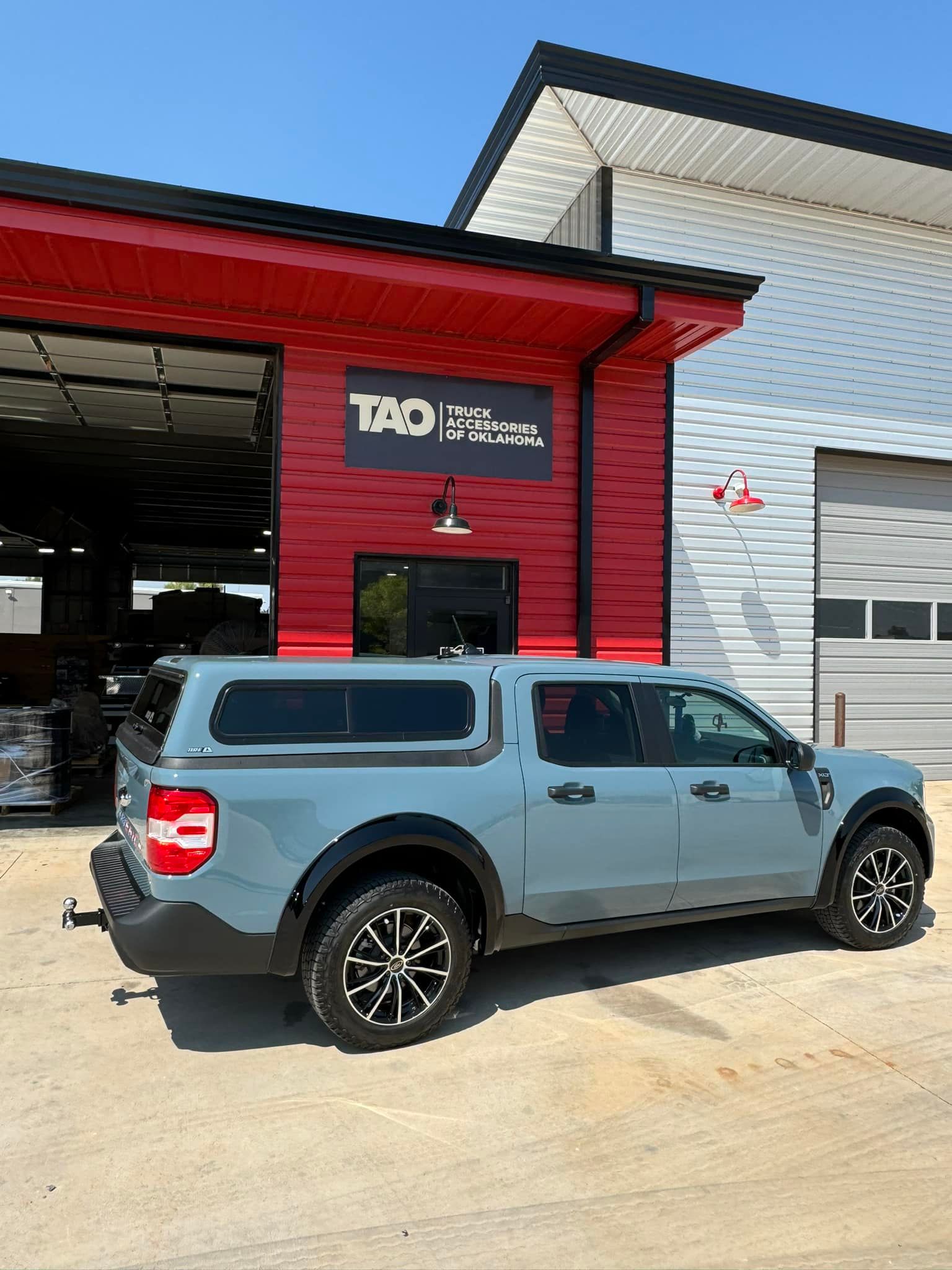Blue pickup truck with canopy parked outside a red and white building.