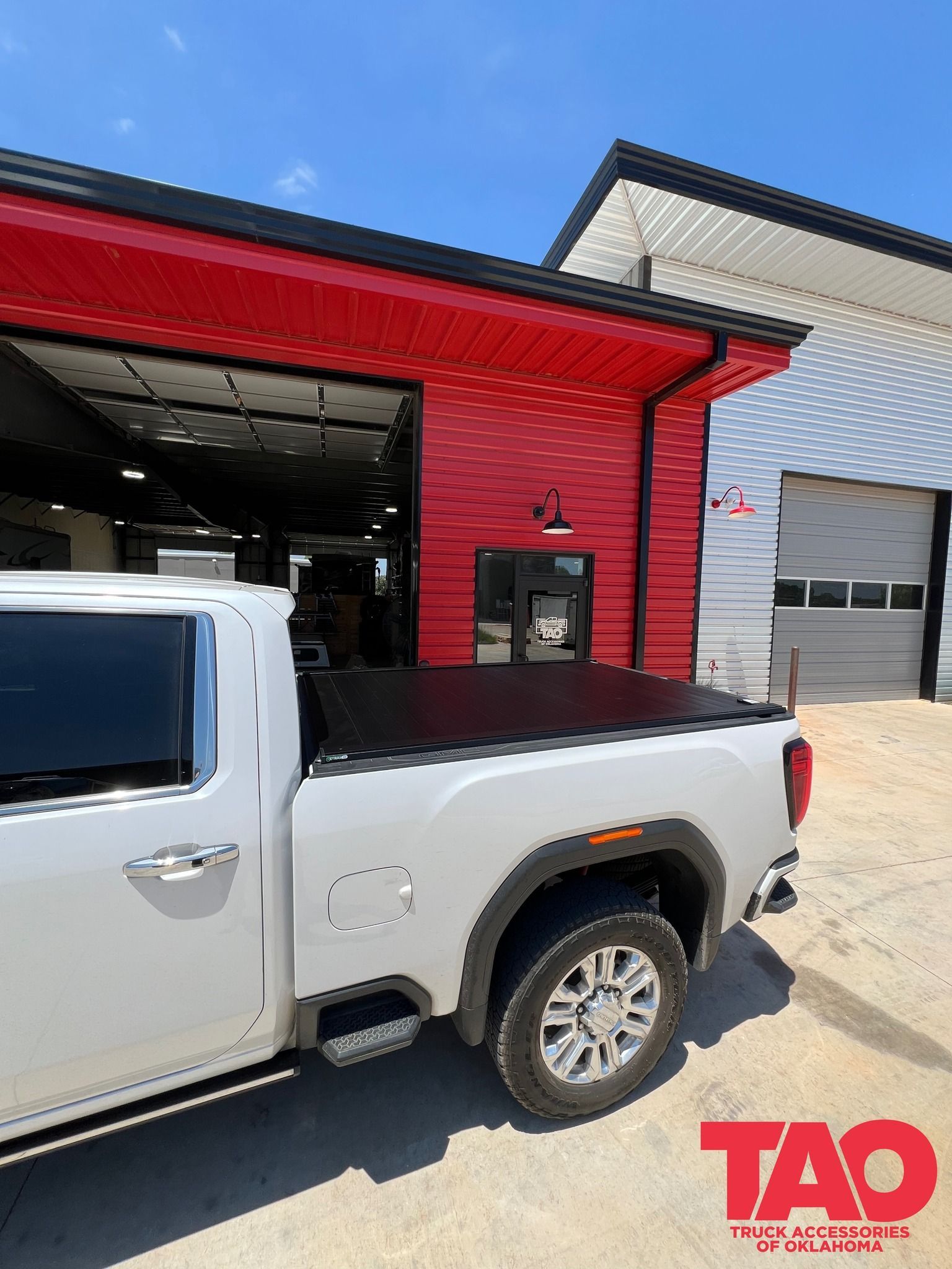 White pickup truck with a black bed cover parked outside a red building with a garage door.