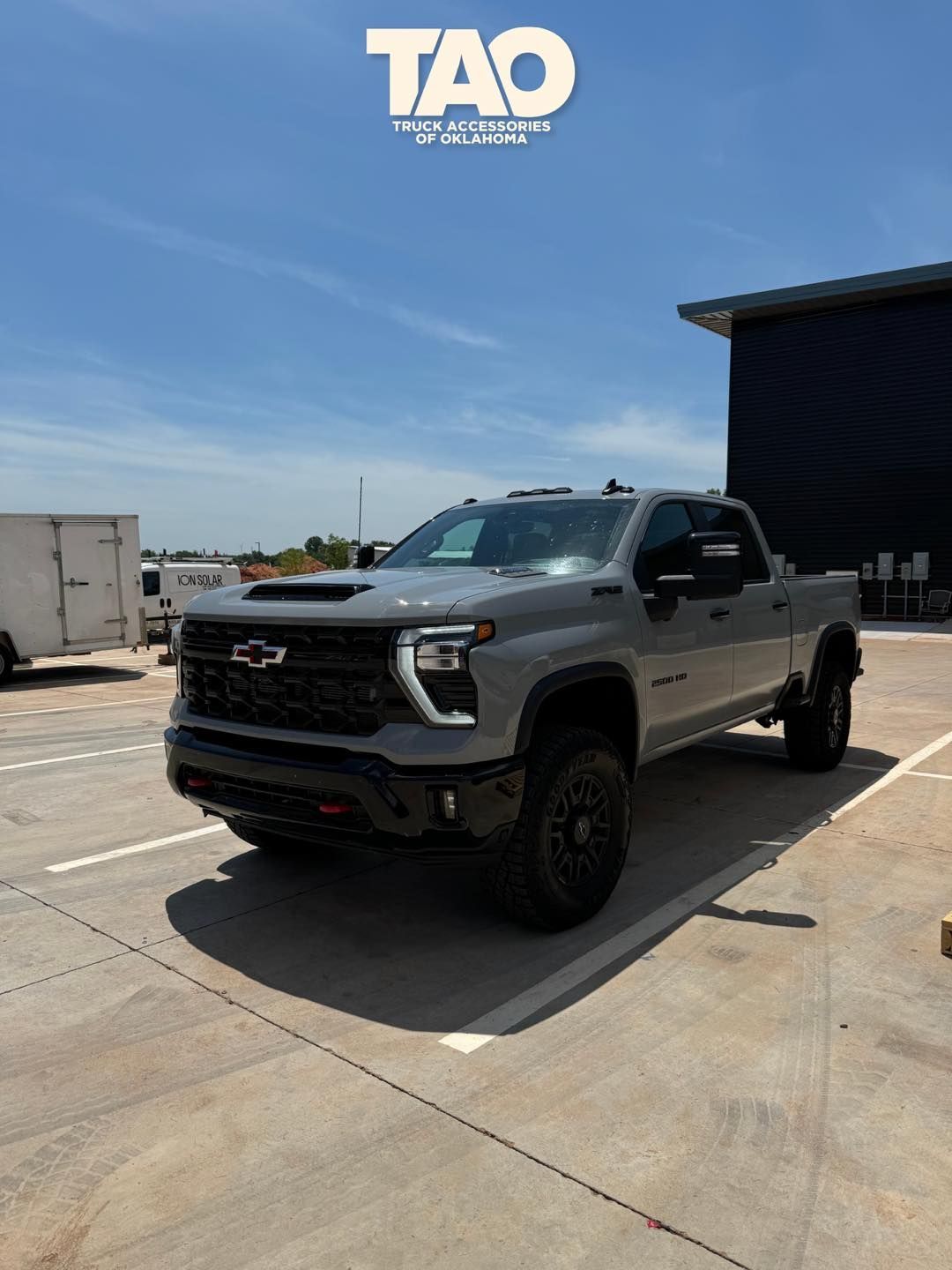 Gray Chevrolet truck parked on pavement under a sunny blue sky.