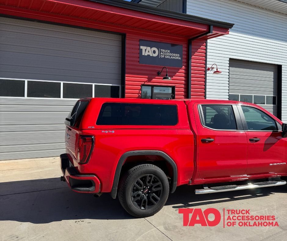 Red truck with a camper shell outside a shop with the sign 