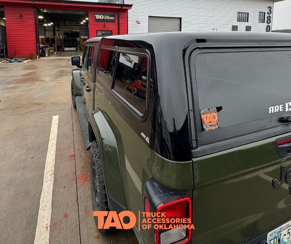 Green Jeep Gladiator with a black topper parked outside a truck accessories shop.