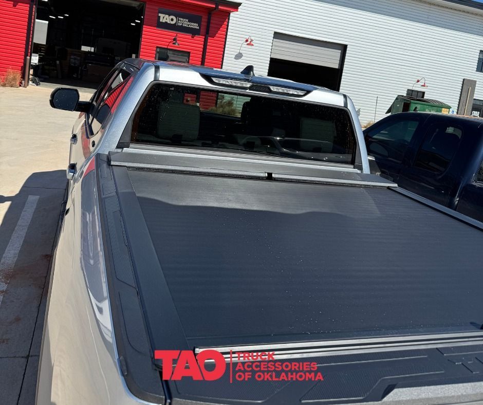 Silver truck with a black tonneau cover parked in front of a building with red accents.