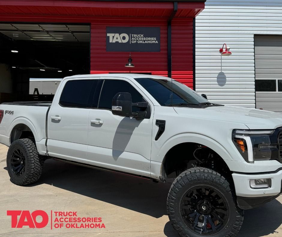 White Ford F-150 truck with black wheels, tinted windows, and lift kit outside 