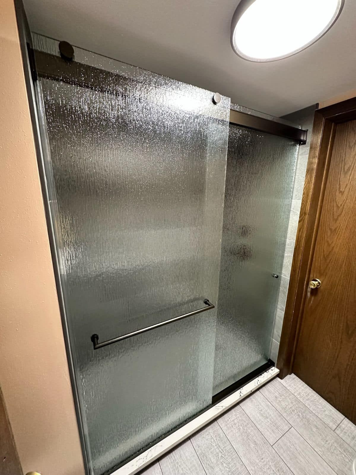 A bathroom with a sliding glass shower door and a wooden door.