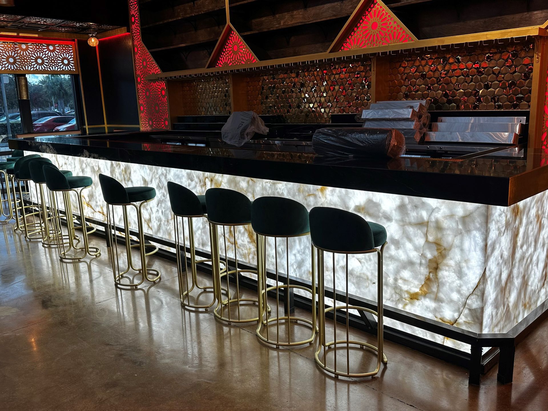 A row of bar stools are lined up in front of a long bar.