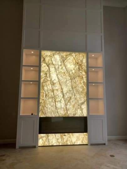 There is a fireplace in the middle of the room with a marble wall behind it.