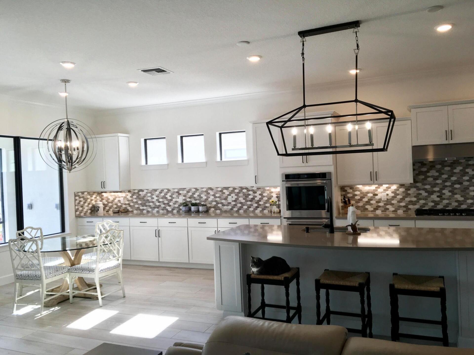 A kitchen with white cabinets , stools , a table and a chandelier hanging from the ceiling.