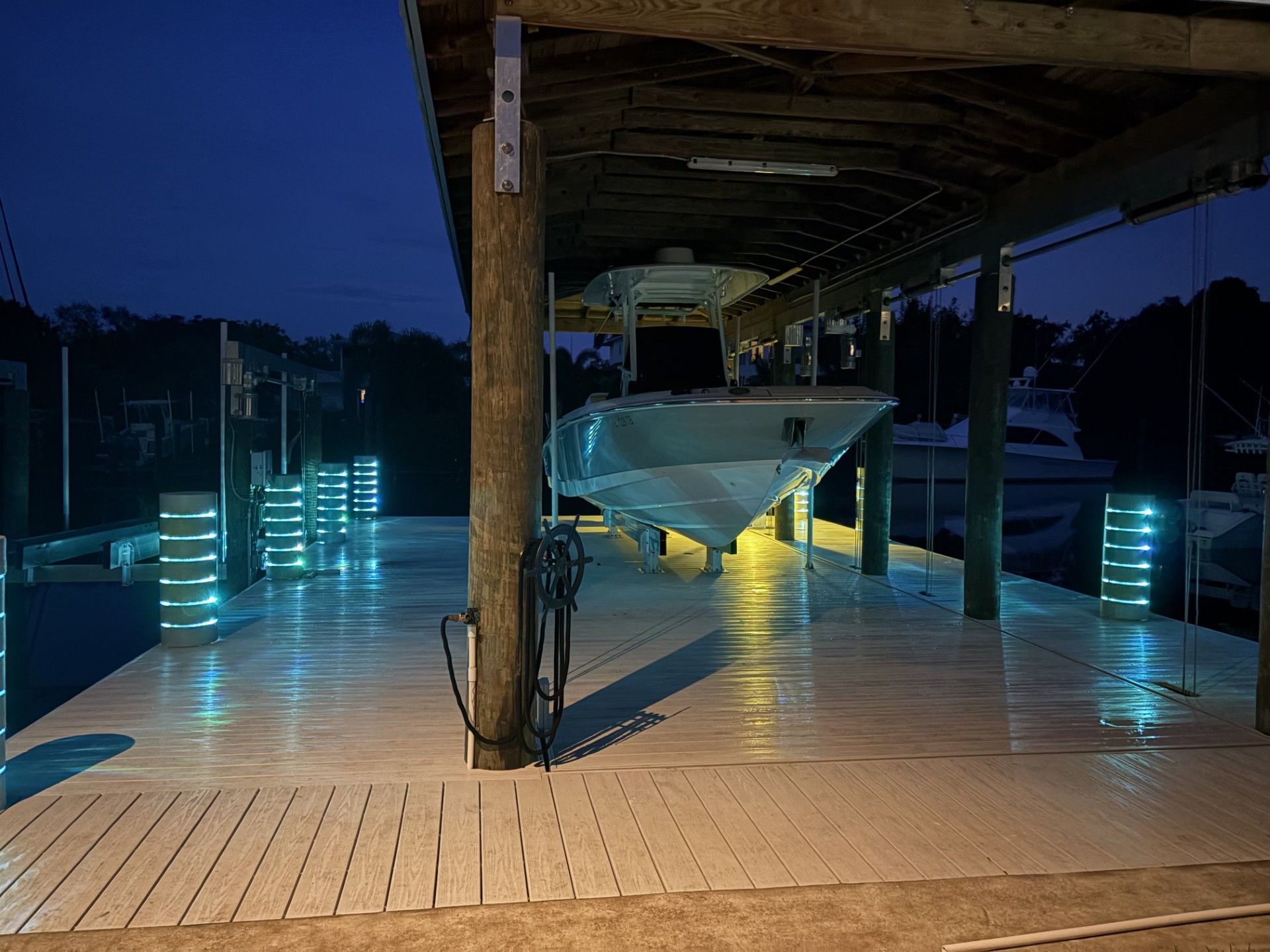 Boat on a covered dock at night; lit with blue and white lights; wooden structure, dark water background. 
