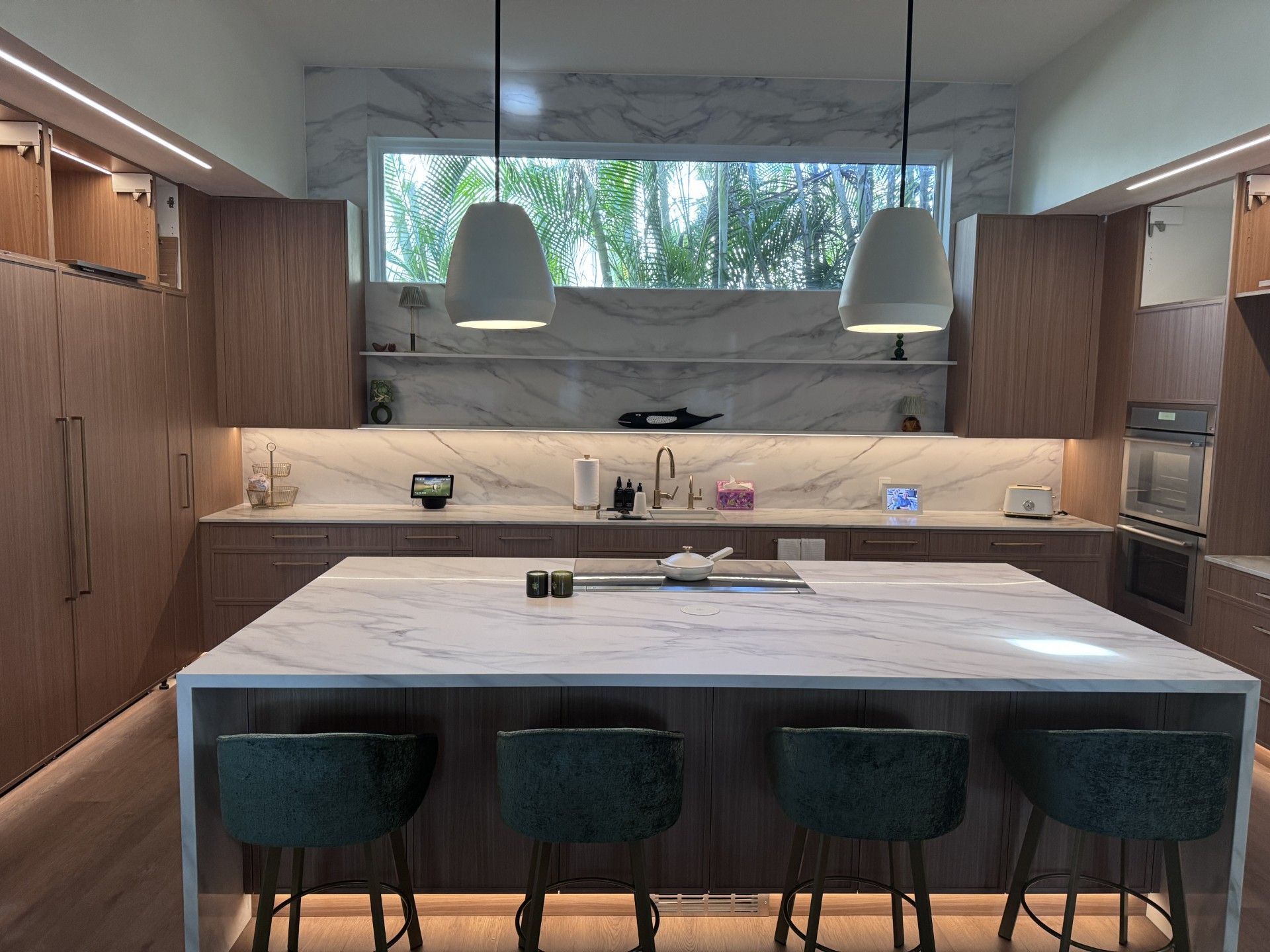 Modern kitchen with wood cabinets, marble countertops, island with bar stools, and pendant lights. 