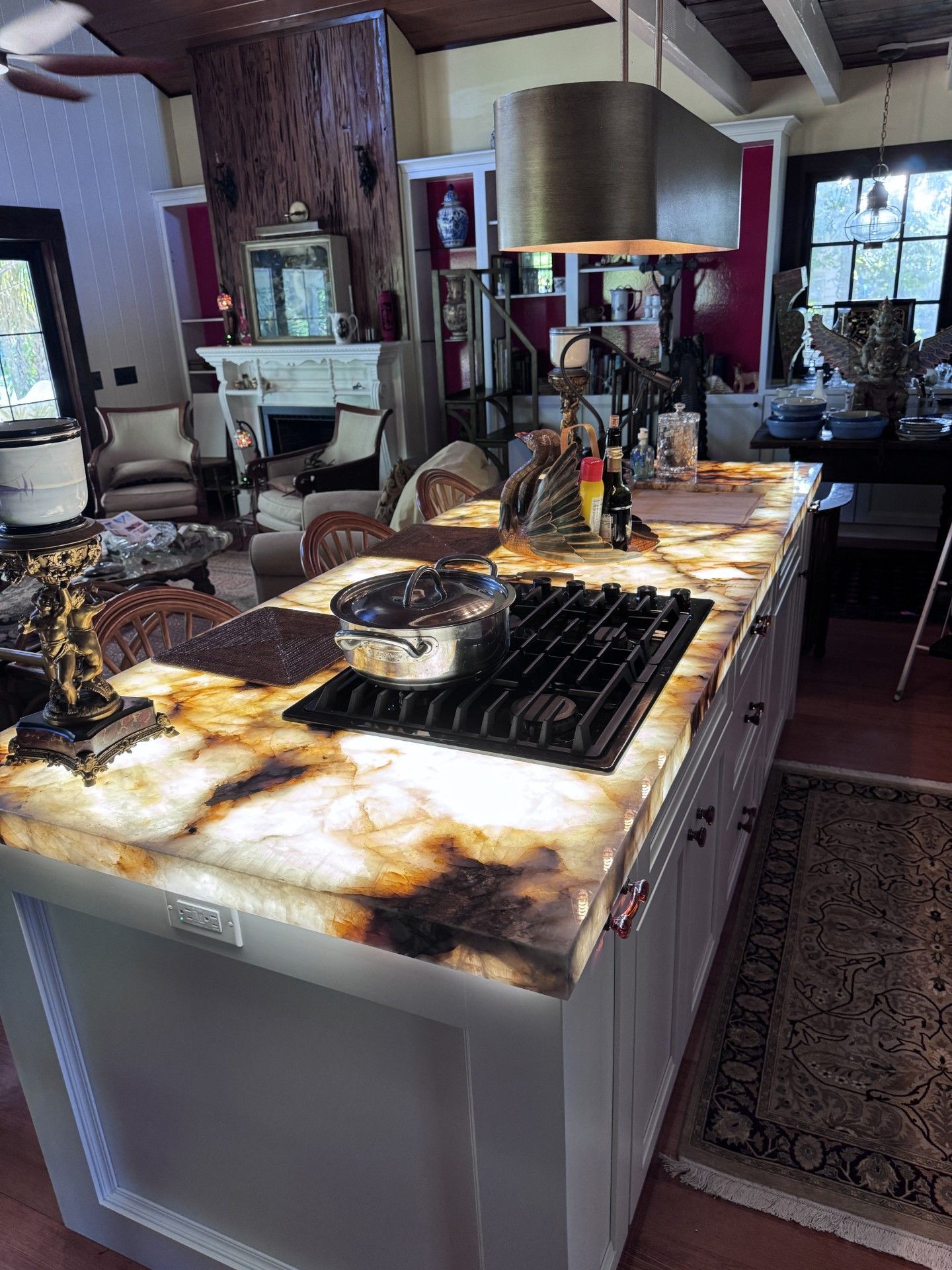 Kitchen island with lit onyx countertop, cooktop, and pot; living room in background. 