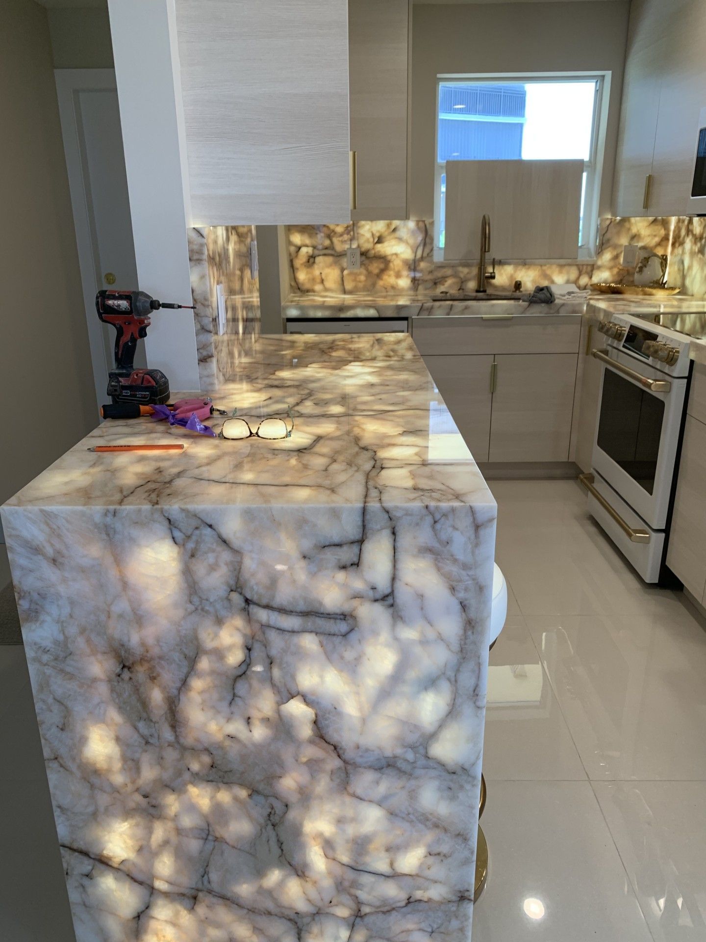 Kitchen with a backlit marble countertop and backsplash, white cabinetry, and stainless steel appliances. 