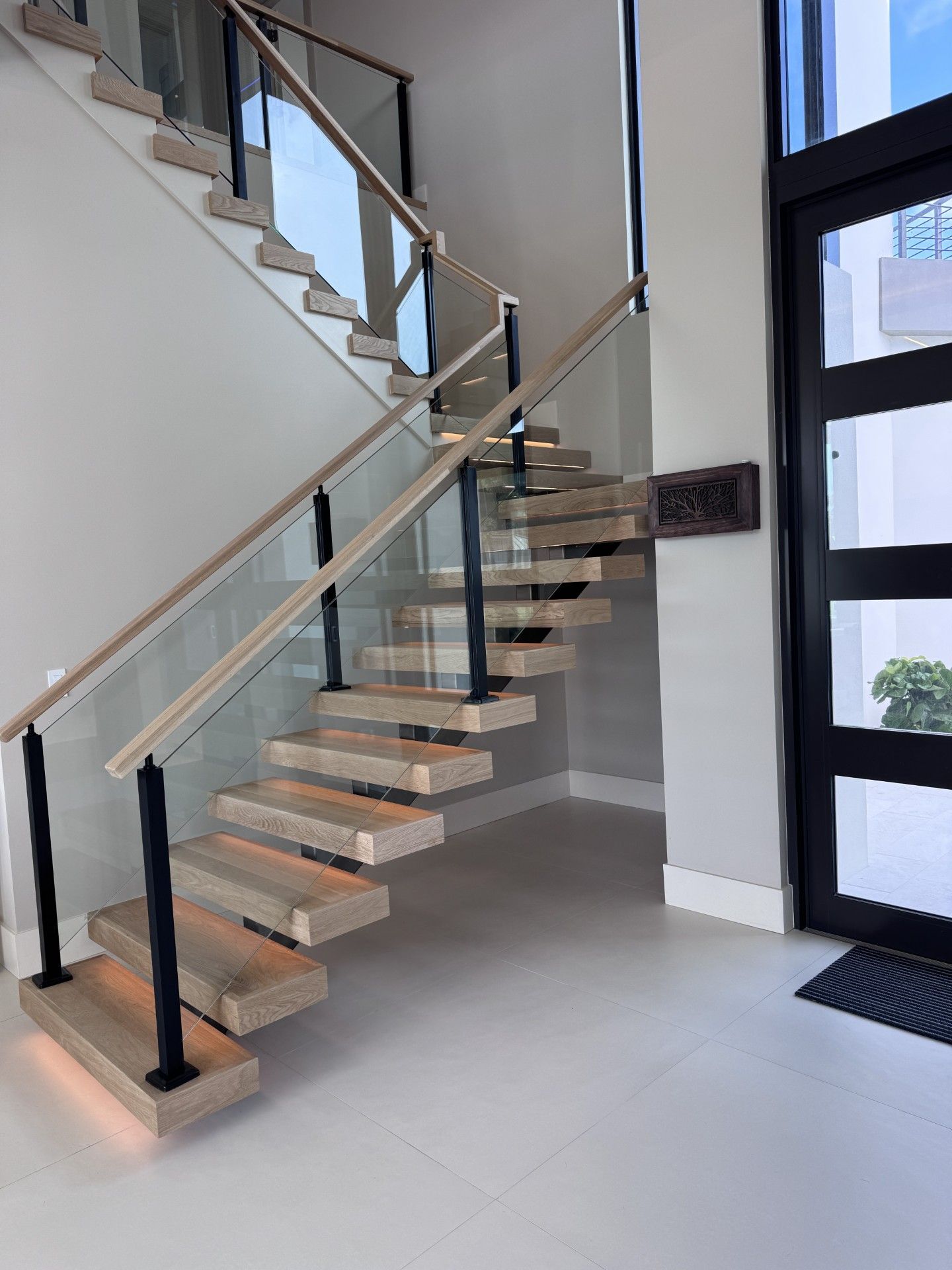 Floating wooden staircase with glass panels, black metal posts, and a door. 