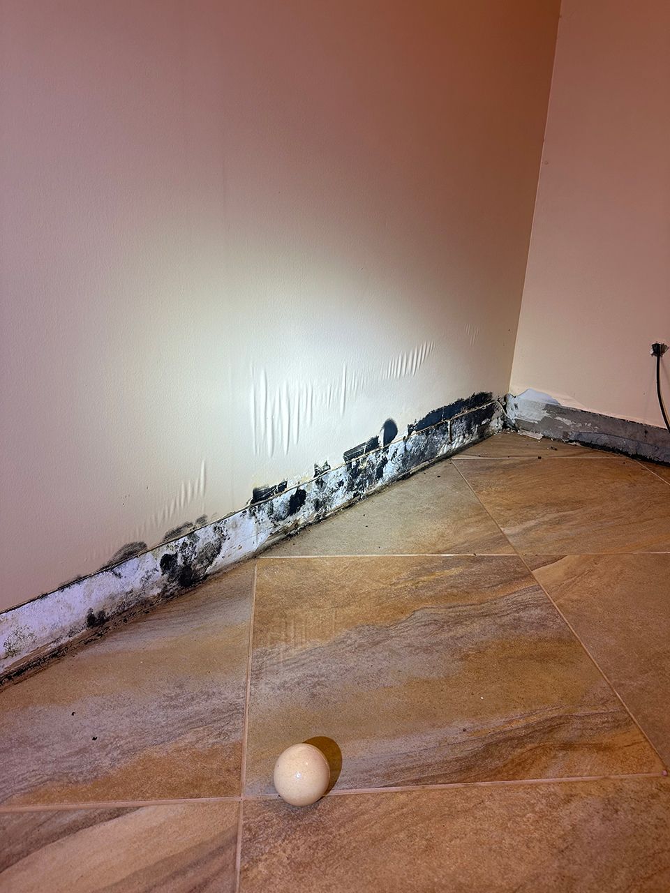 A white ball is sitting on a tiled floor next to a wall with molds
