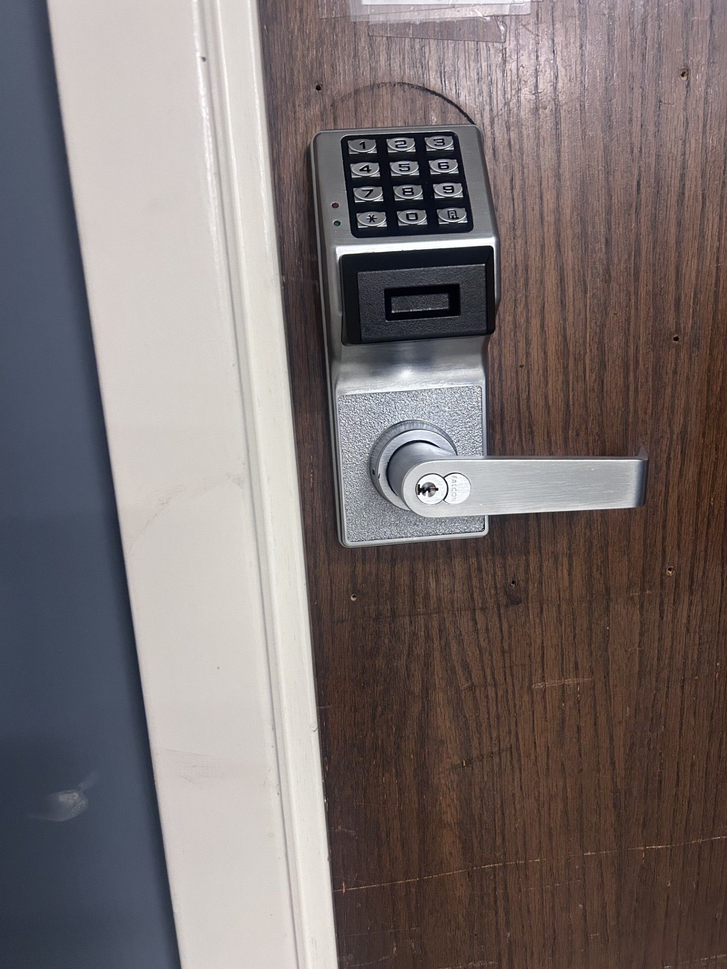 Electronic keypad door lock on a brown wooden door with a silver handle and keyhole.