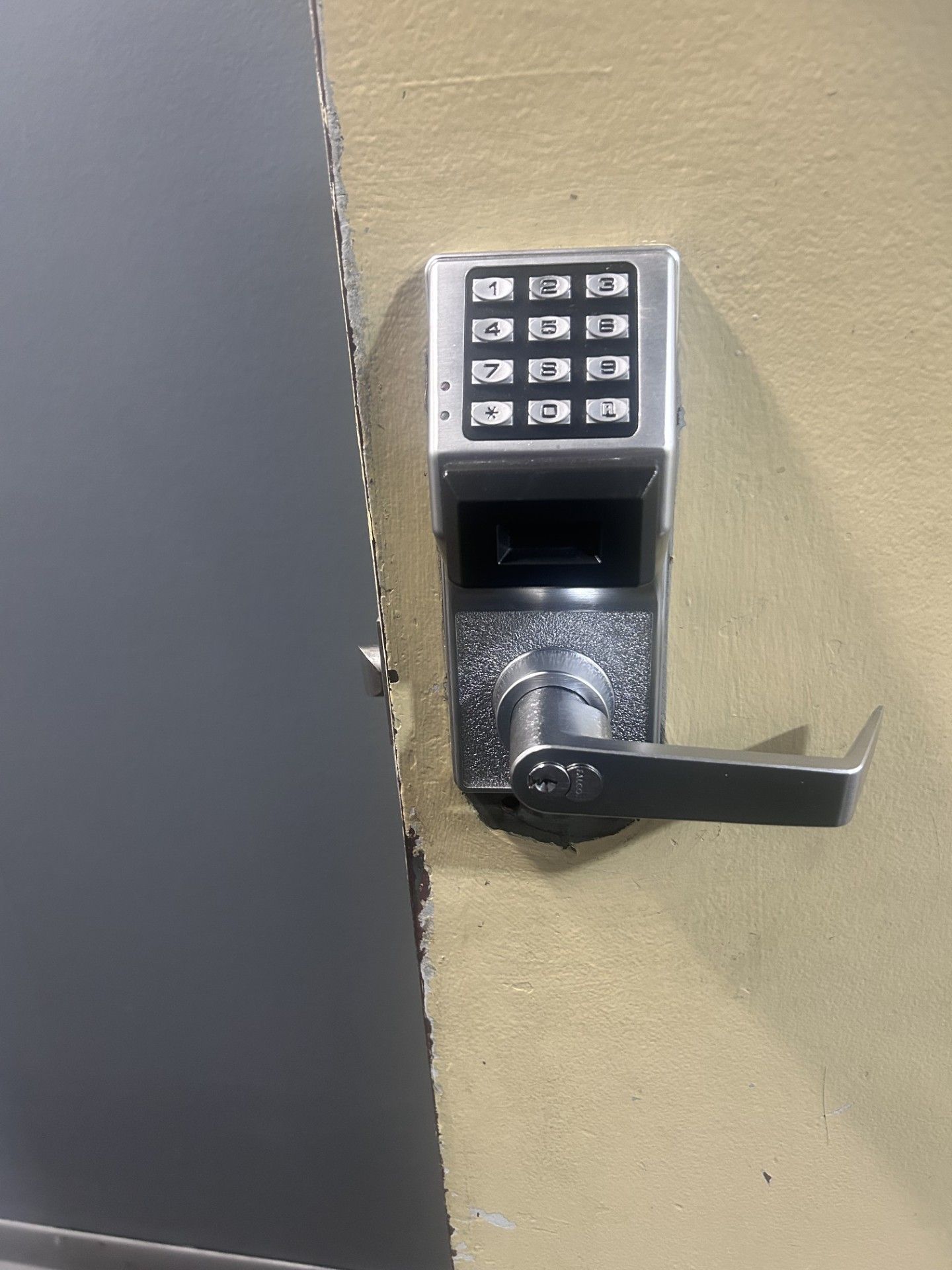 Digital keypad door lock on a beige wall next to a grey door.