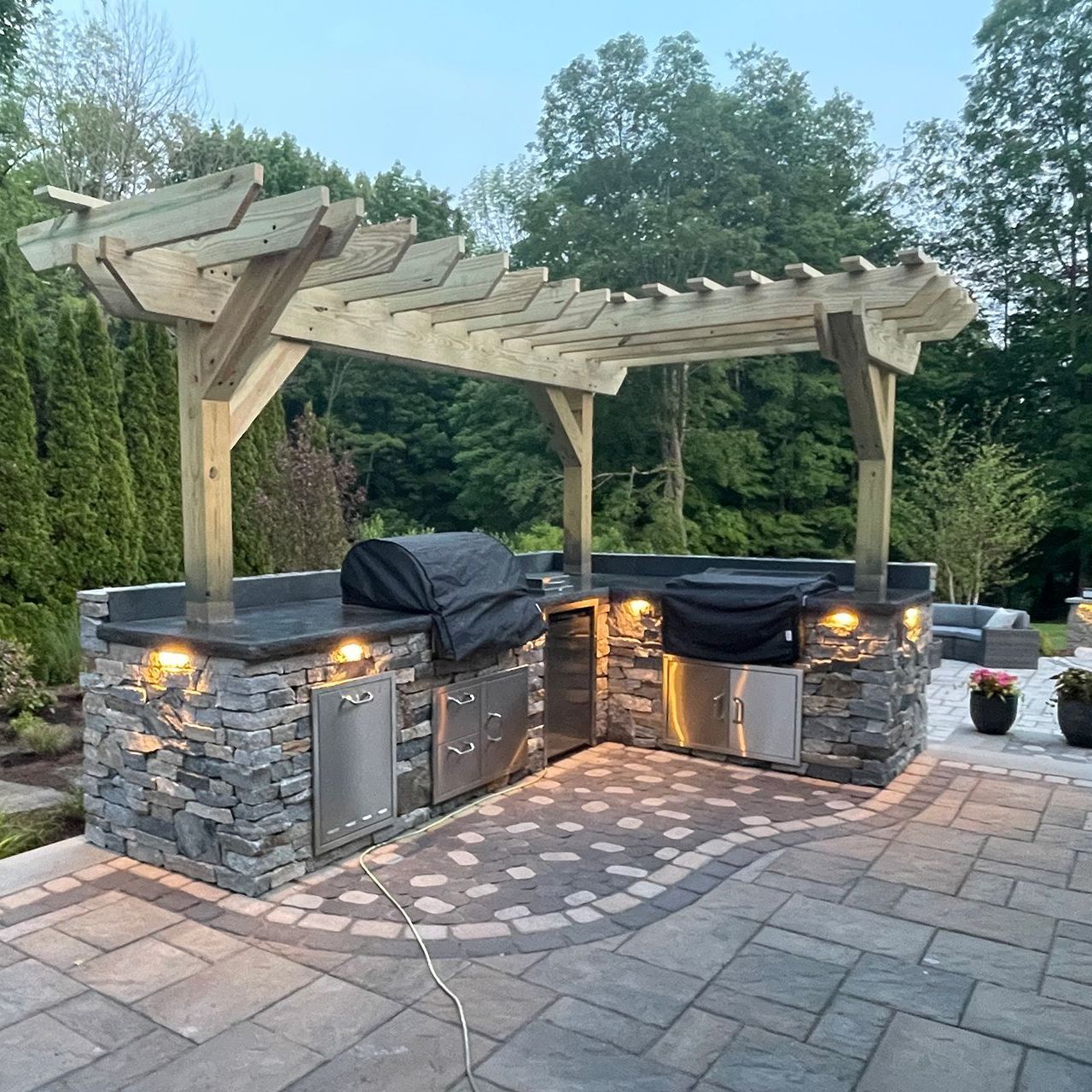 An outdoor kitchen with a grill under a pergola