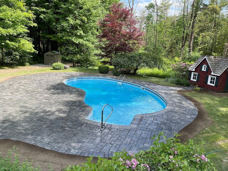 A large swimming pool is surrounded by a brick patio and a red shed.