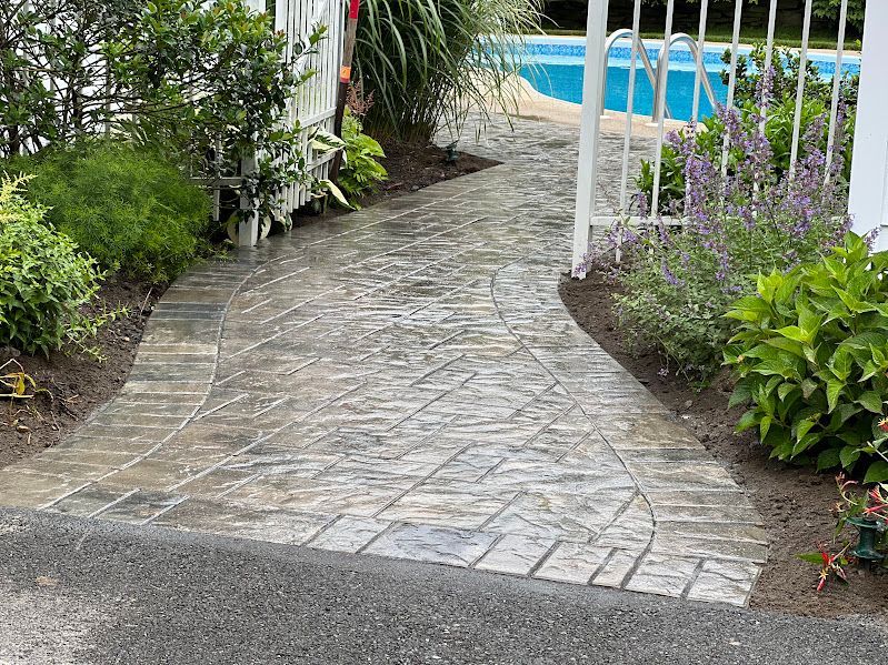 A brick walkway leading to a pool in a backyard.