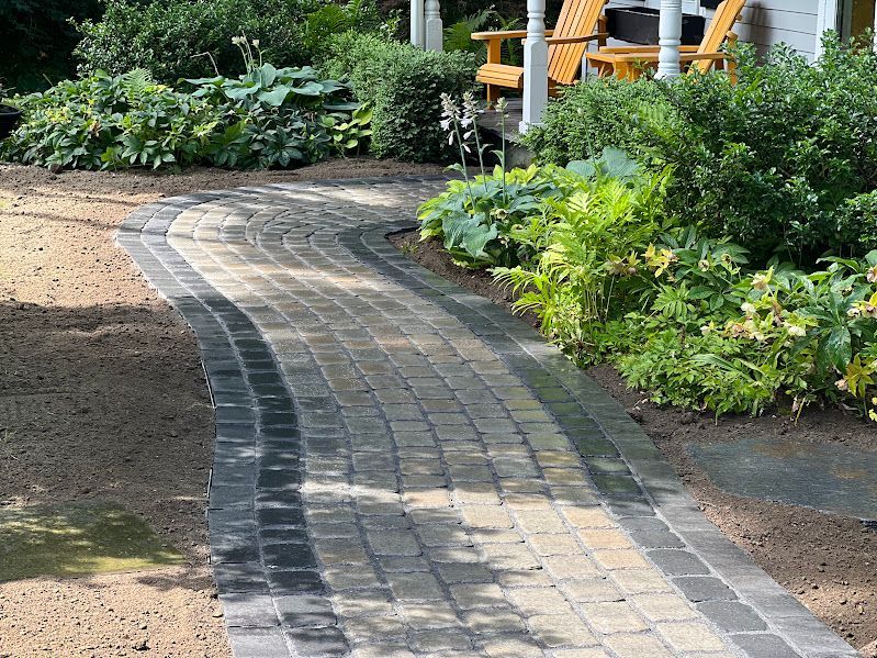 A brick walkway leading to a house with a porch and chairs.