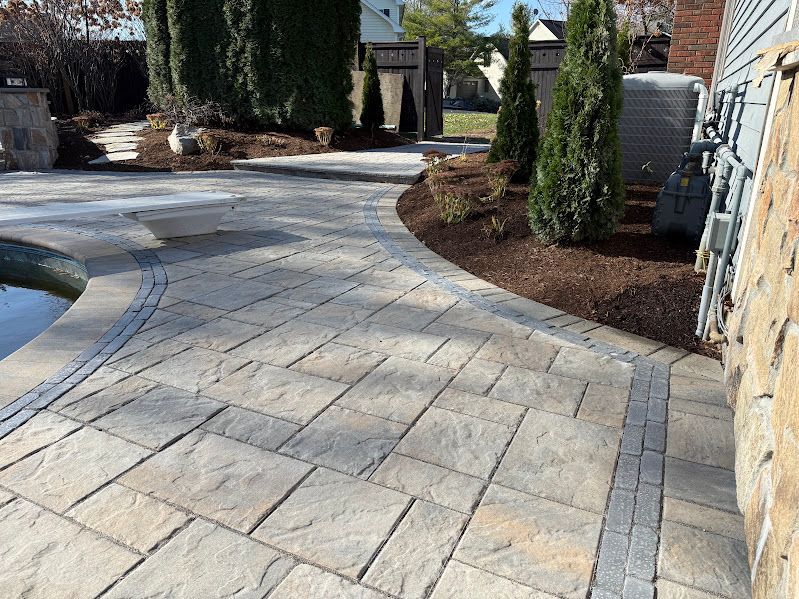 A brick walkway leading to a pool in a backyard.