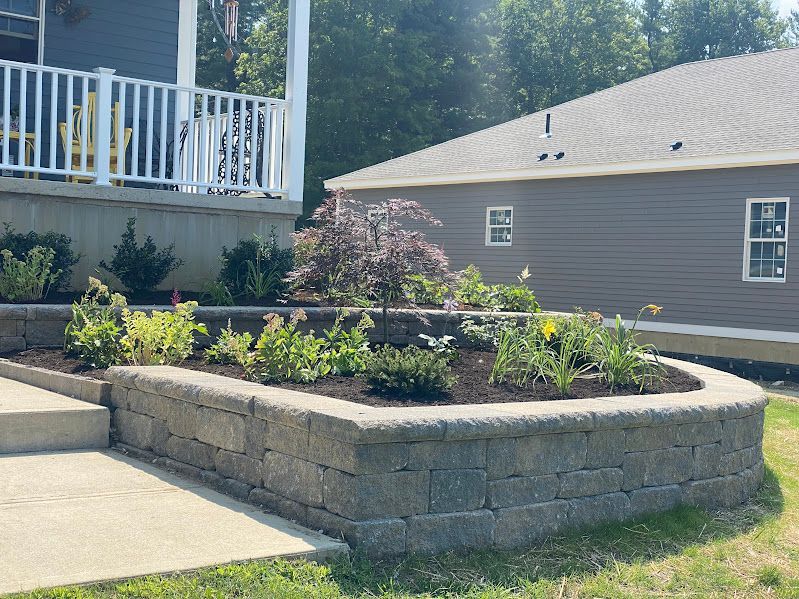 A brick wall with plants in it in front of a house.