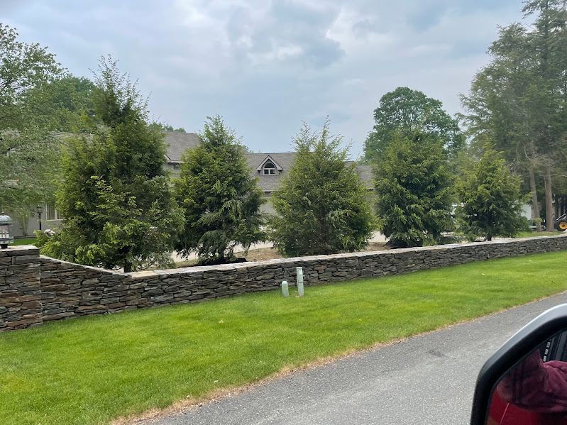 A stone wall surrounds a lush green lawn in front of a house.