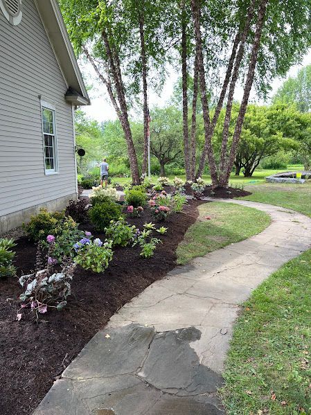 A walkway leading to a house with a lot of flowers and trees.