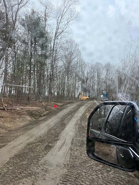 A car is driving down a dirt road in the woods.