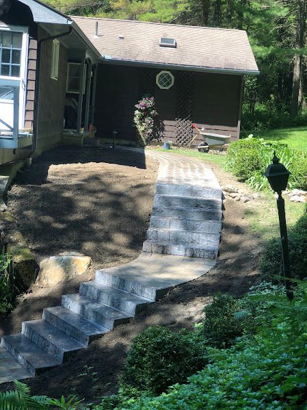 A stone walkway leading to a house with stairs leading up to it.