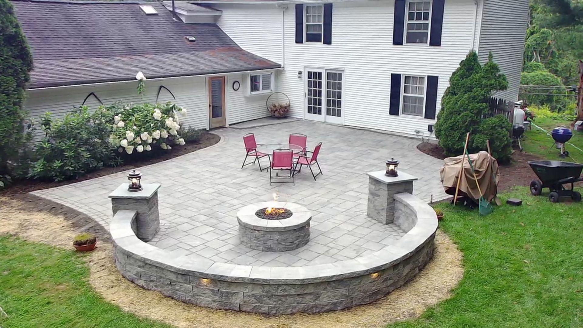 A patio with a fire pit and chairs in front of a house.