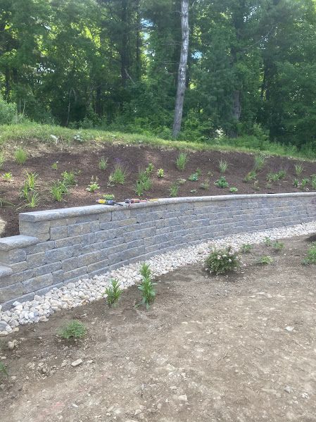 A stone wall is sitting on top of a dirt hill next to a forest.