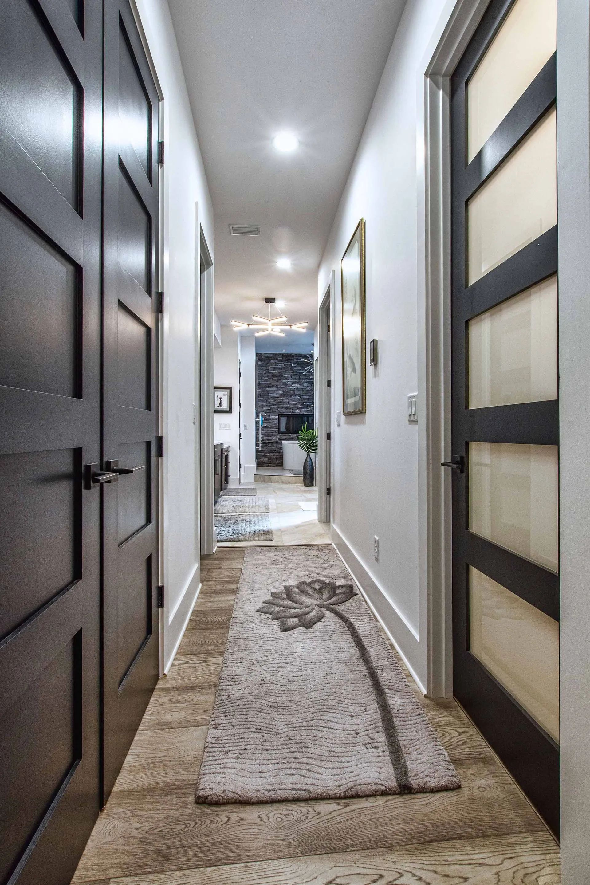 A long hallway with black doors and a rug on the floor.
