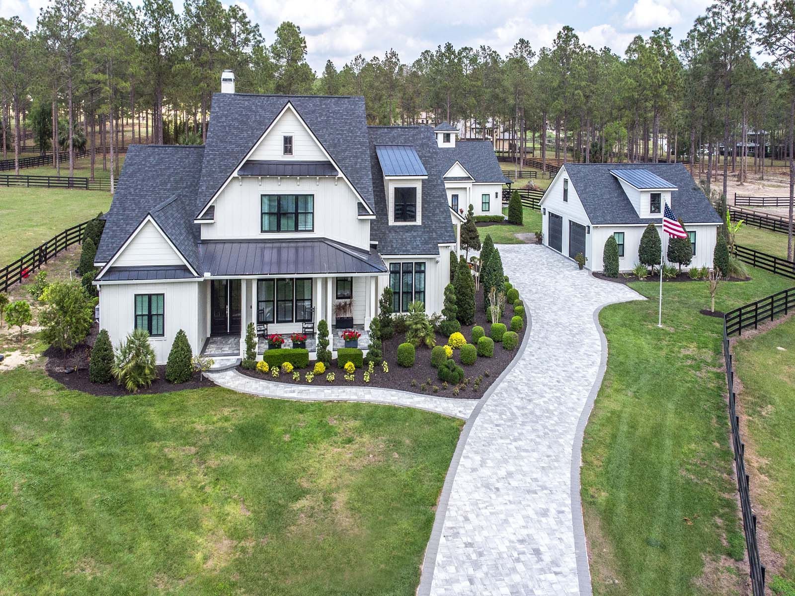 A white house with a black roof is sitting on top of a lush green field.