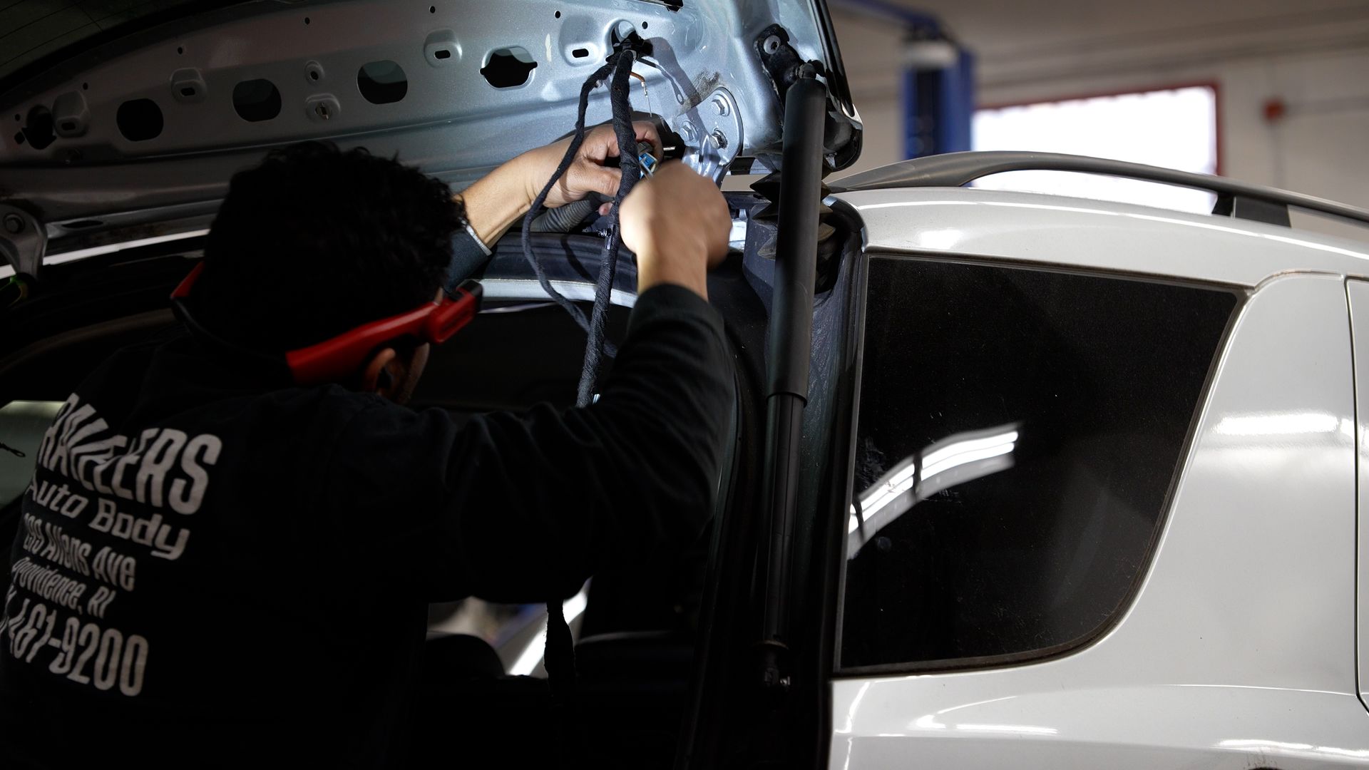 Person installing wiring on a white SUV inside a garage.
