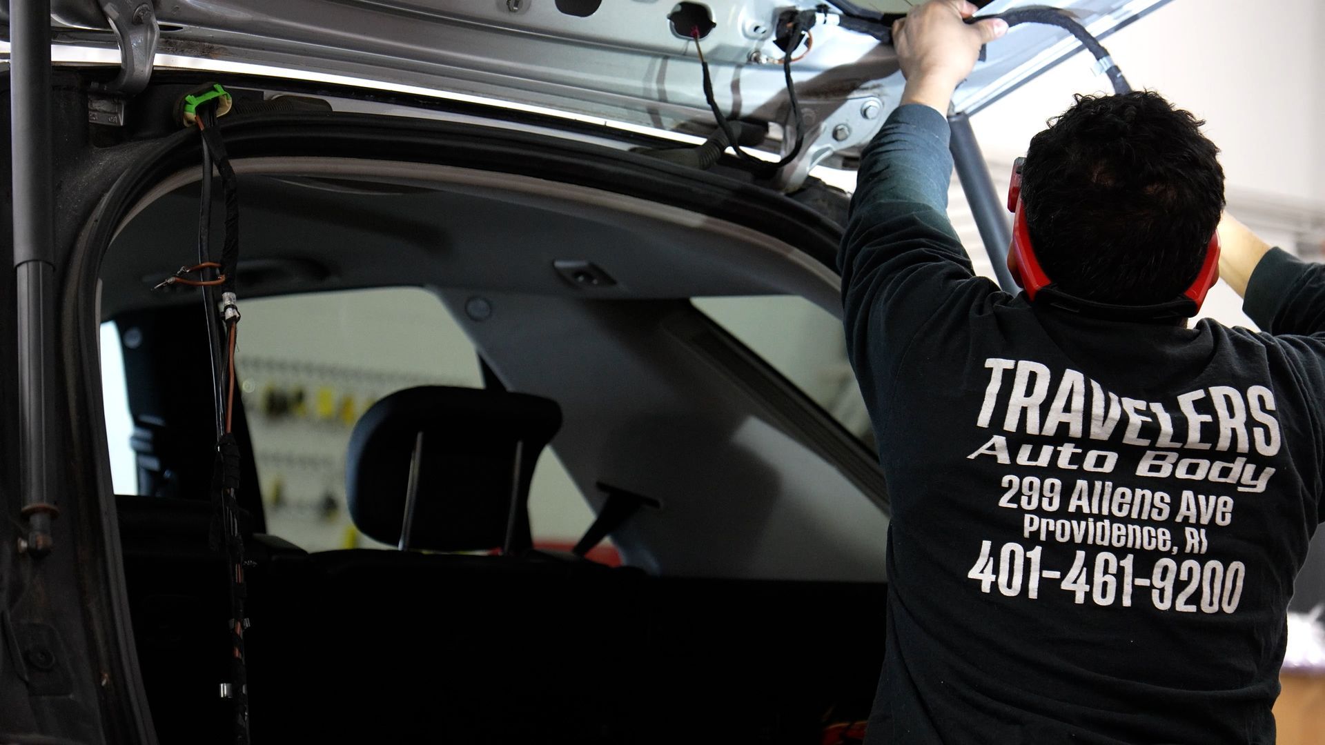 Worker in a black shirt installing trim inside a vehicle with the rear hatch open.