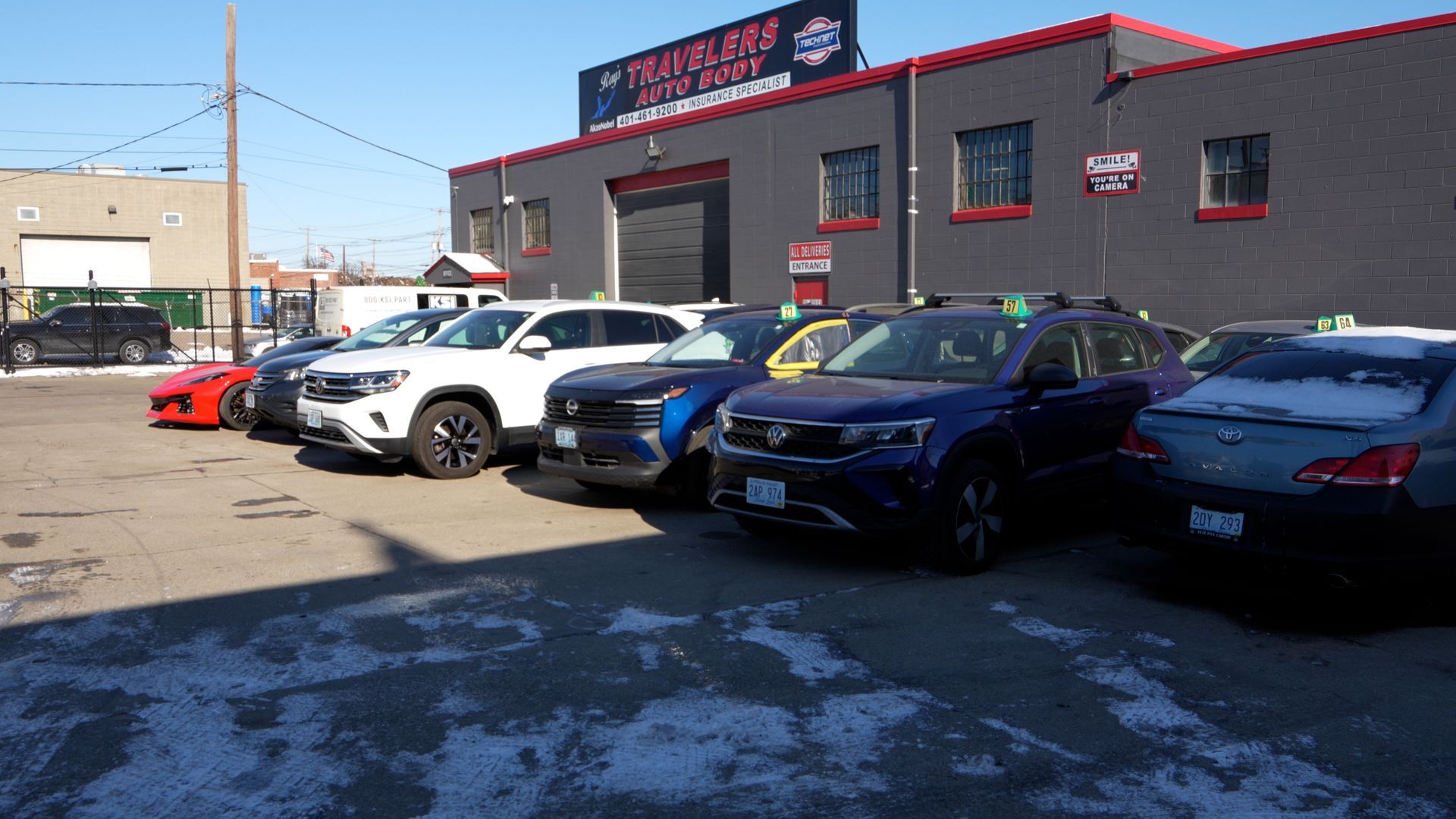 Car lot with several parked vehicles beside a gray building under a clear blue sky.