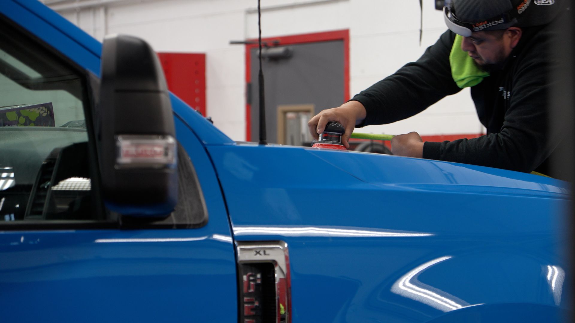 A mechanic is polishing the blue truck's body panel in a workshop.