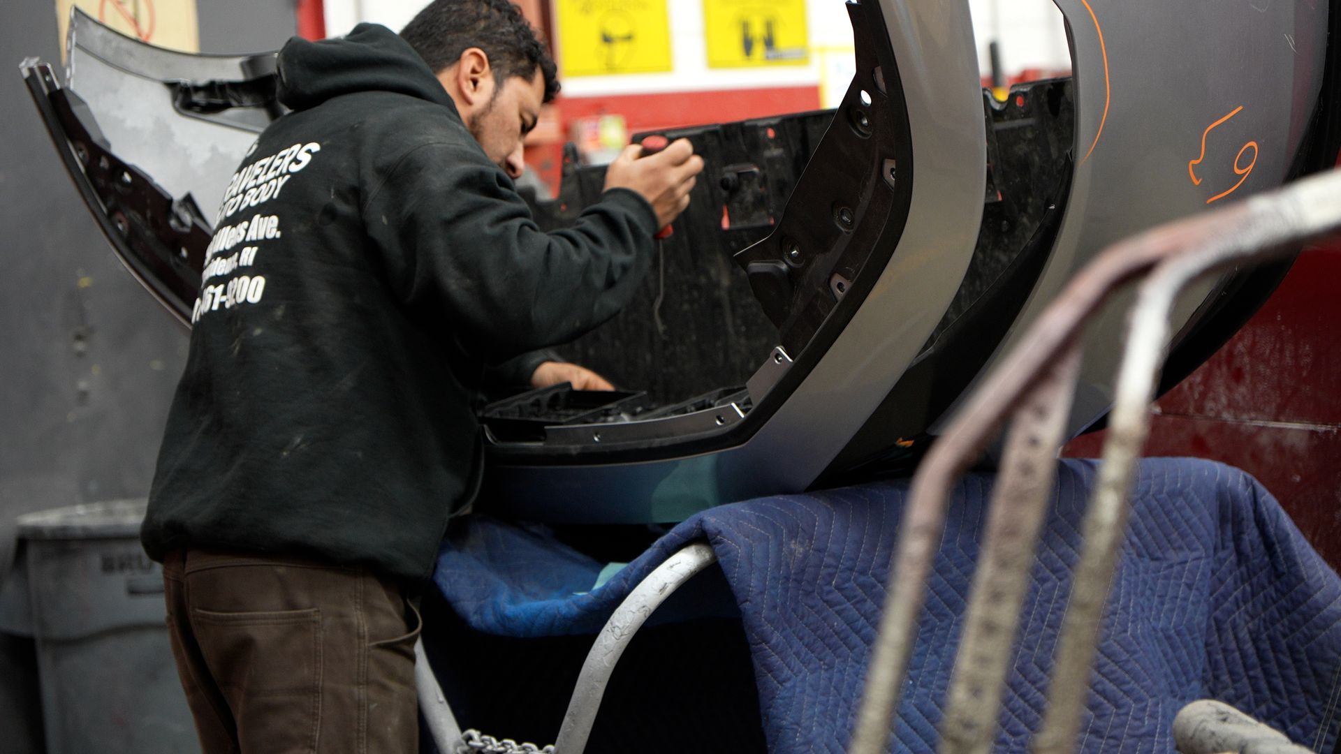 Worker inside a large black cylindrical machine, reaching into its opening in a workshop.