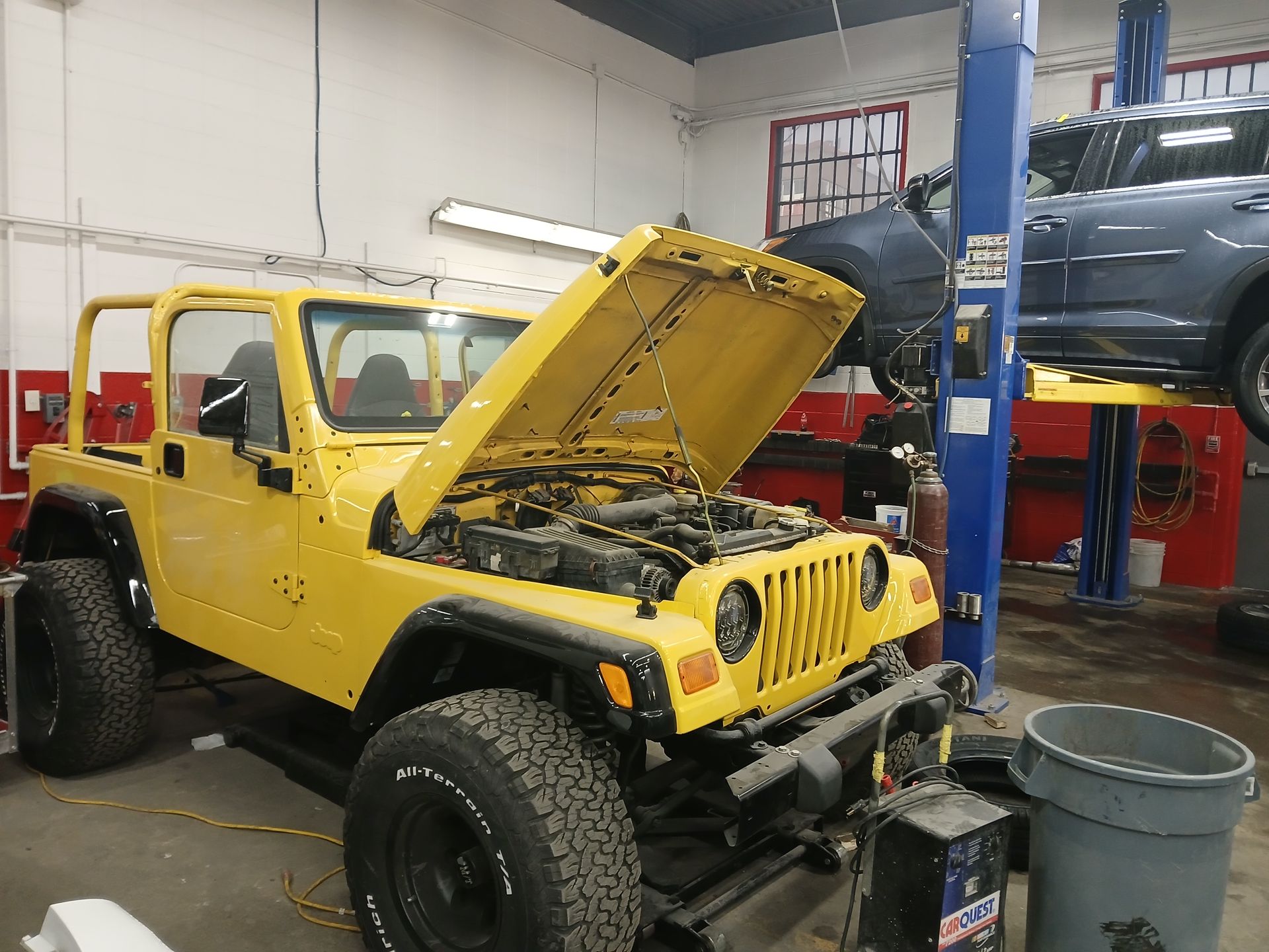 A yellow jeep is parked in a garage with its hood up.
