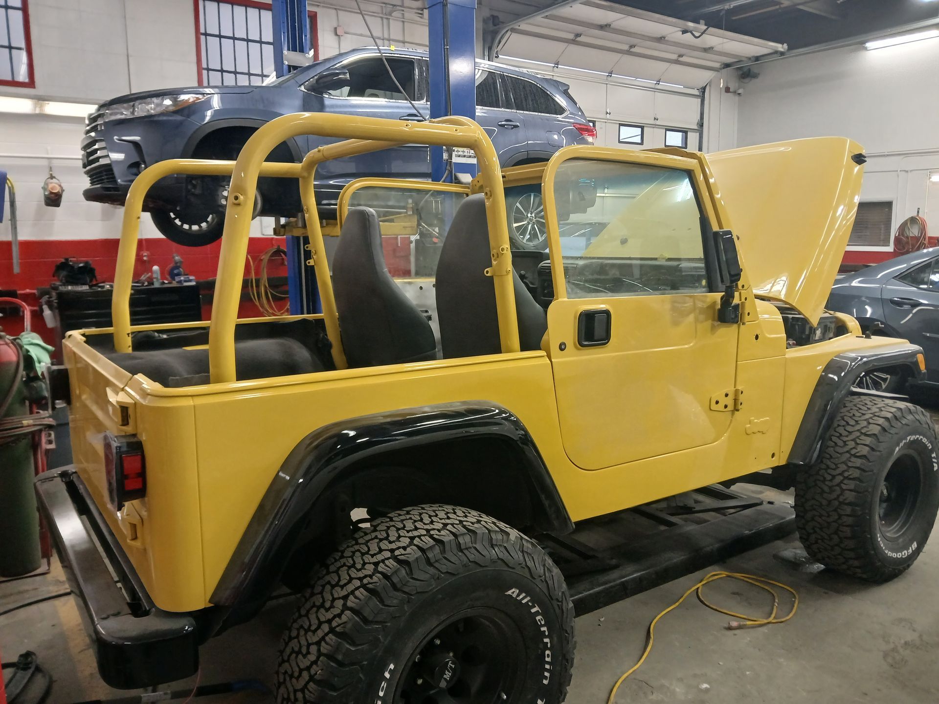 A yellow jeep is parked in a garage with the hood open.